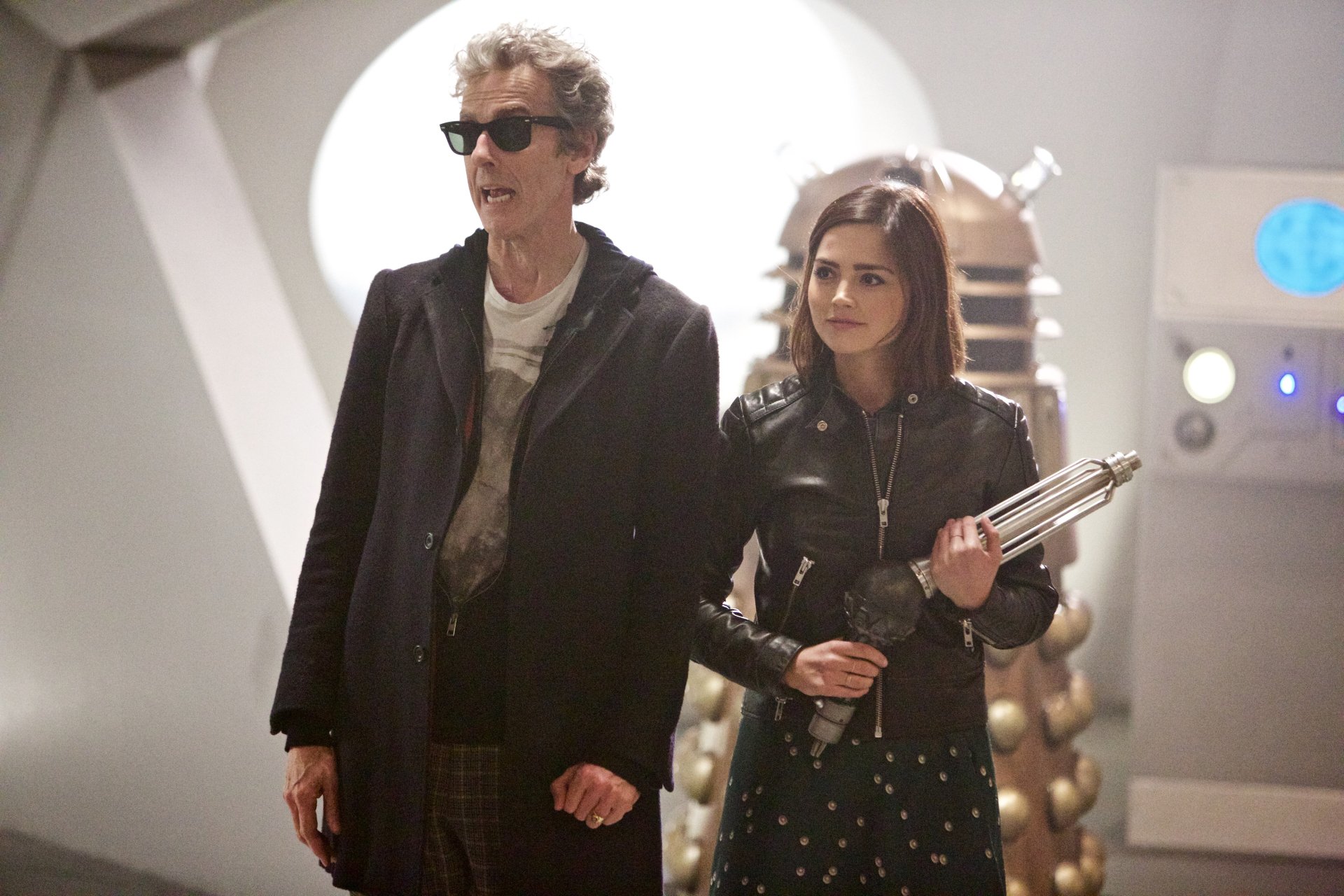 Peter Capaldi as the 12th Doctor and Jenna Coleman as Clara Oswald walk together with a Dalek behind them, from the TV show Doctor Who (2005) in a 4K Ultra HD wallpaper.