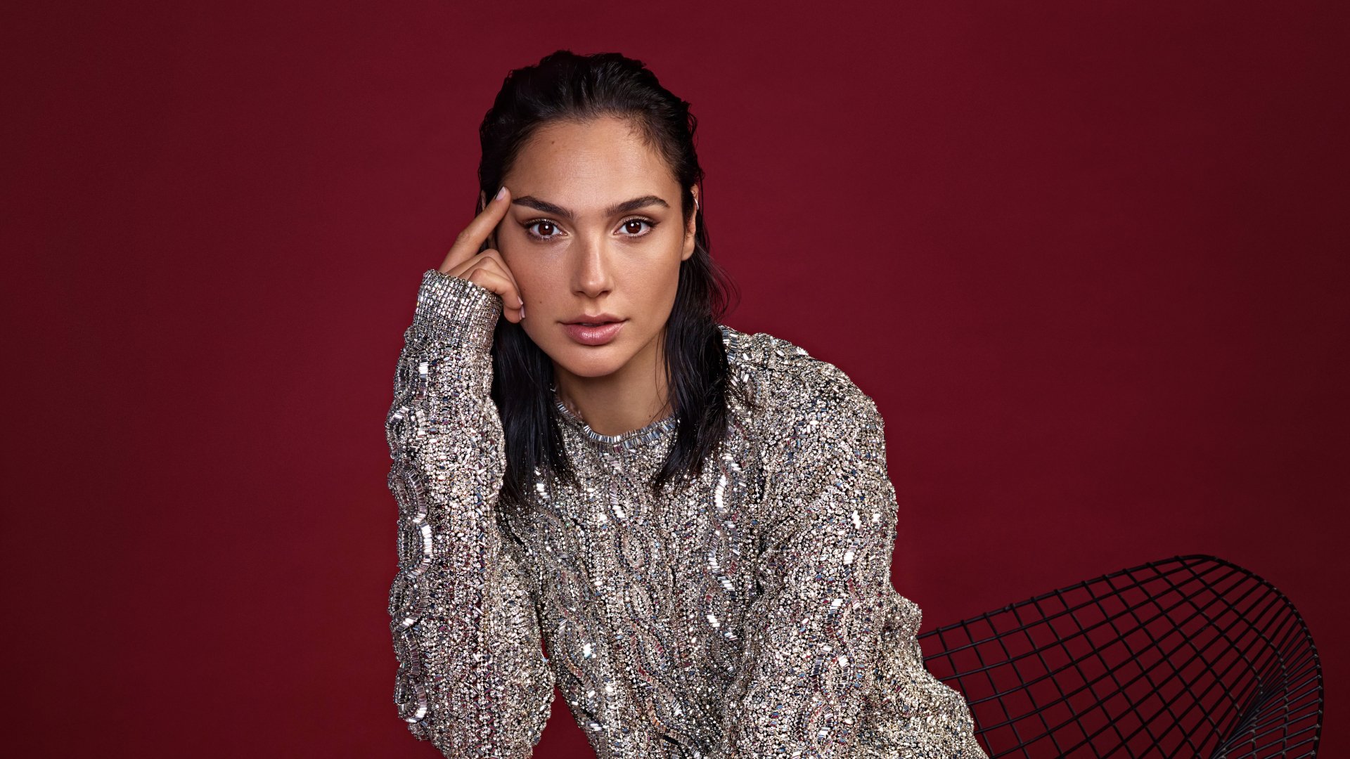 Portrait of Israeli actress Gal Gadot with black hair and brown eyes, wearing a textured silver sweater against a deep red background in 4K Ultra HD quality.