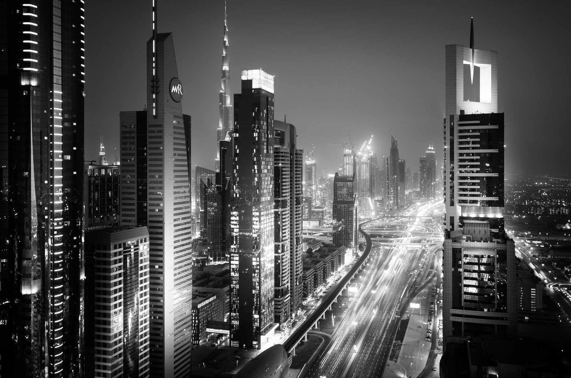 Black and white nighttime cityscape of Dubai featuring illuminated skyscrapers and busy roads, captured in a monochrome HD desktop wallpaper.