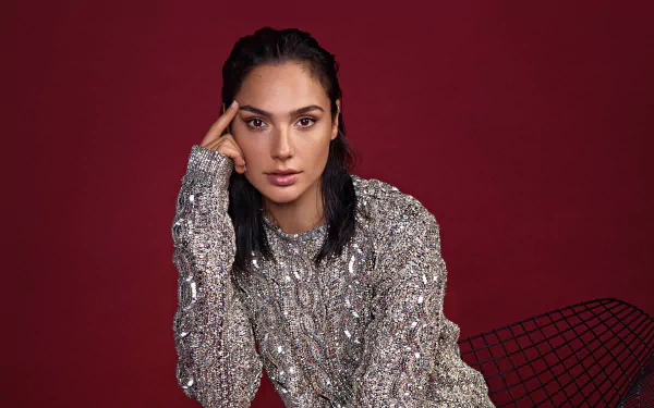 Portrait of Israeli actress Gal Gadot with black hair and brown eyes, wearing a textured silver sweater against a deep red background in 4K Ultra HD quality.