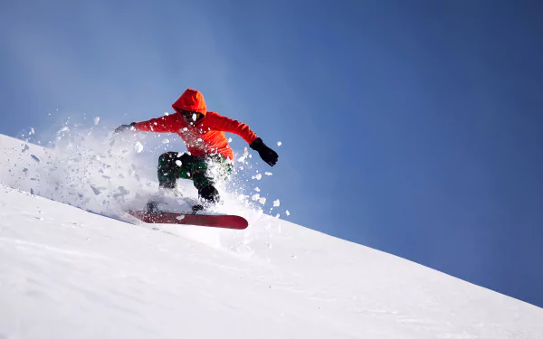 Snowboarder in orange jacket spraying powder down a snowy slope under a clear blue sky — snowboarding sports action, 2K Quad HD PC desktop wallpaper and background.