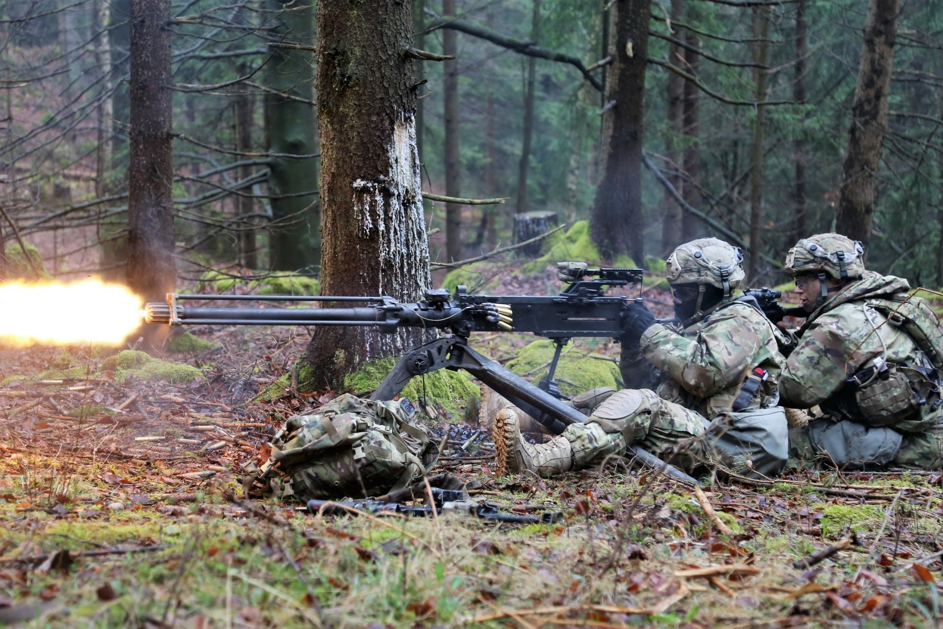 HD desktop wallpaper showing soldiers in military gear firing a machine gun weapon in a dense forest setting.