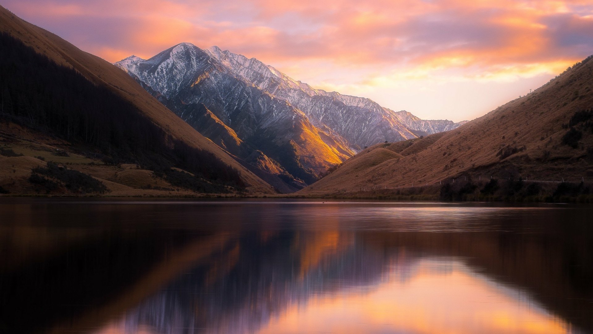 HD desktop wallpaper showcasing a tranquil lake and mountain landscape during a stunning sunset in New Zealand. The scene features vibrant colors and reflects the serene beauty of nature.