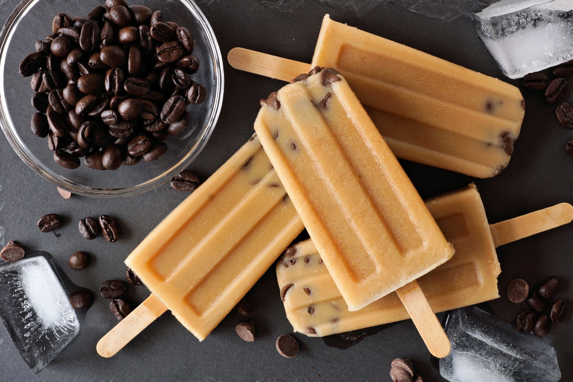 A 4K Ultra HD still life featuring coffee bean popsicles with scattered coffee beans and ice cubes on a dark surface, combining ice cream and coffee elements.