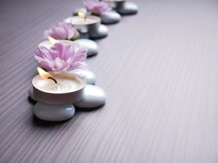 Close-up 4K Ultra HD photo of zen candles resting on smooth stones, with delicate pink flowers arranged along a textured surface, creating a calm desktop wallpaper background.