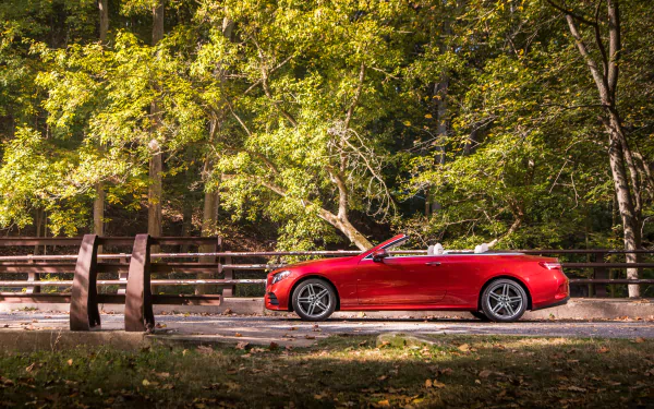 Red Mercedes-Benz E-Class cabriolet parked beside a wooden fence in a lush, green forest, captured in 4K Ultra HD for a PC desktop wallpaper.