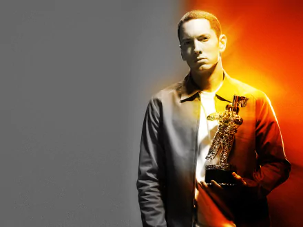 HD desktop wallpaper of a brown-eyed rapper holding a gold trophy against a split gray-to-orange background, wearing medals and a serious expression.