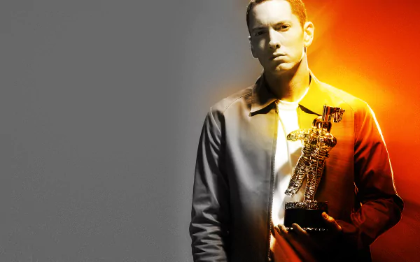 HD desktop wallpaper of a brown-eyed rapper holding a gold trophy against a split gray-to-orange background, wearing medals and a serious expression.