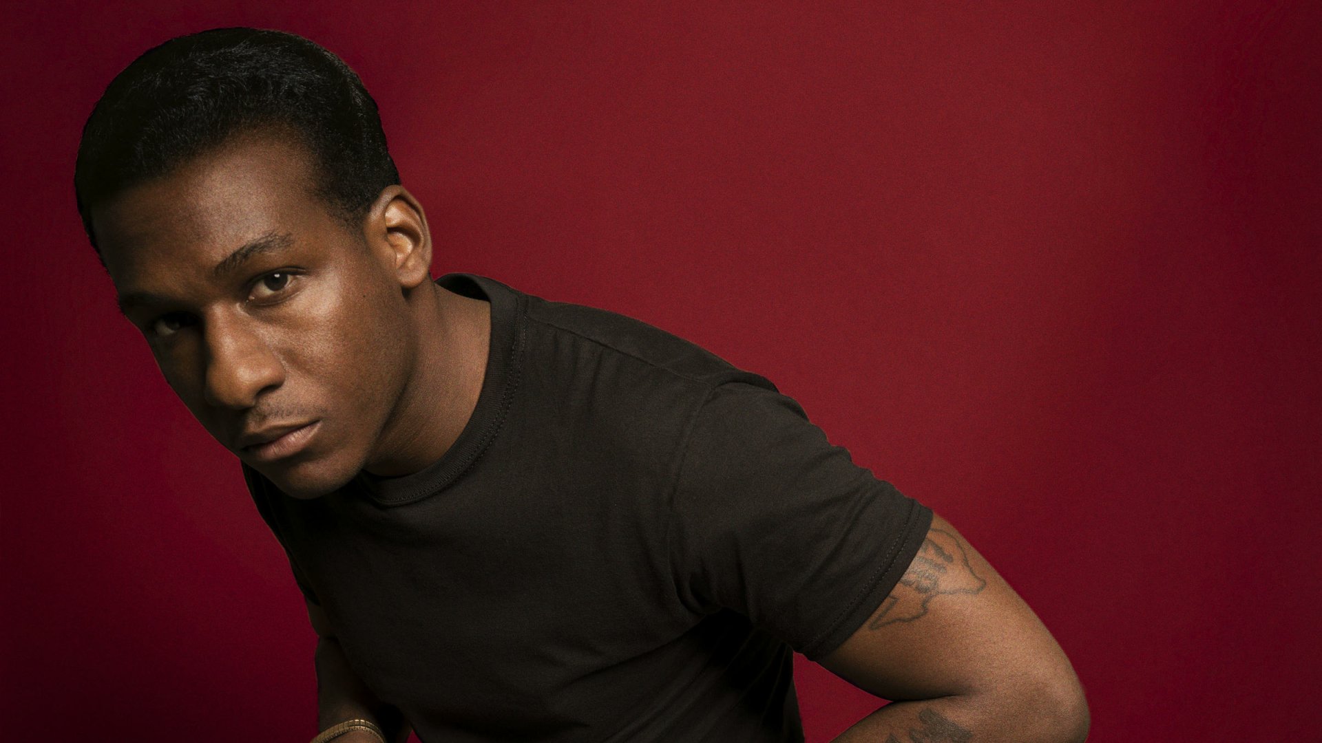 HD desktop wallpaper featuring a man with a serious expression, wearing a black shirt against a red background.