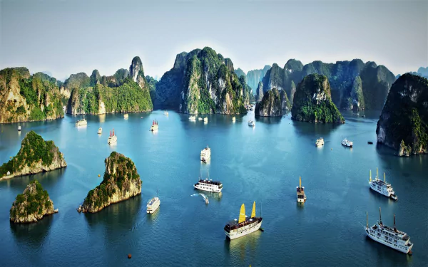 HD desktop wallpaper showcasing boats sailing through the emerald waters of Ha Long Bay, Vietnam, surrounded by towering limestone karsts in the ocean.