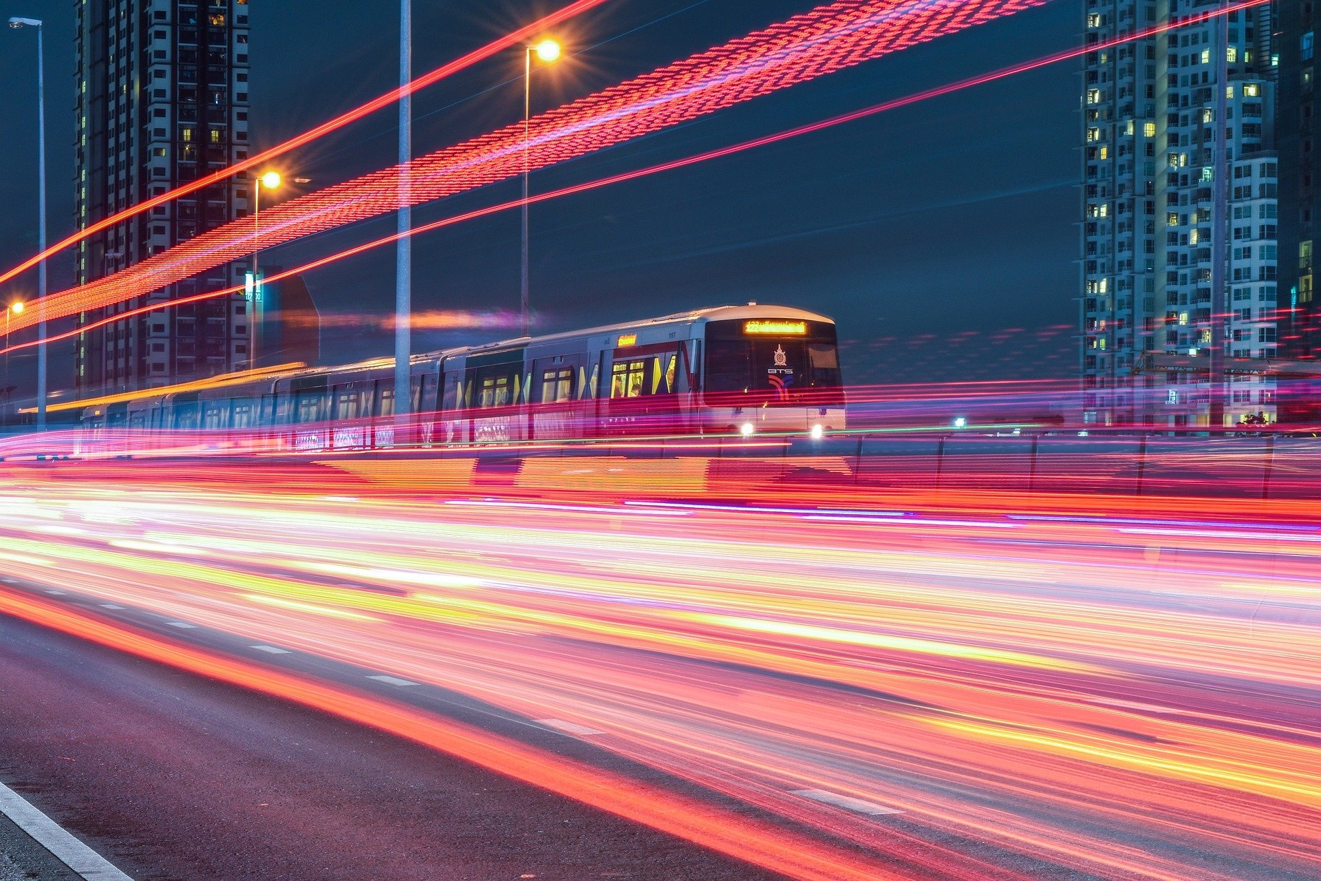 Time-lapse HD wallpaper of a train passing through a cityscape at night, with streaks of light from moving vehicles creating a dynamic and vibrant effect.