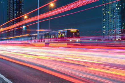 Time-lapse HD wallpaper of a train passing through a cityscape at night, with streaks of light from moving vehicles creating a dynamic and vibrant effect.