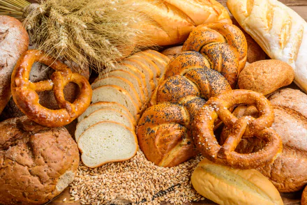 5K Ultra HD PC desktop wallpaper showing assorted breads and pretzels — sliced loaf, rolls, poppy-seed twists and wheat stalks in a rustic baking food still life.
