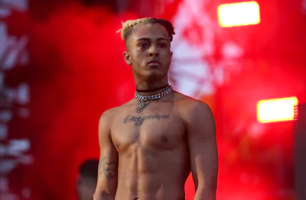 HD desktop wallpaper featuring XXXTentacion shirtless against a vibrant red backdrop at a music event.