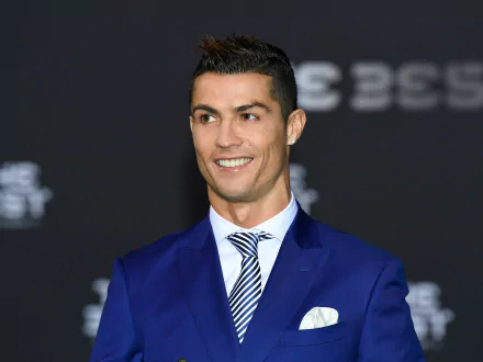Cristiano Ronaldo, the Portuguese soccer star, smiles while wearing a blue suit and striped tie. The image serves as a high-definition desktop wallpaper and background.
