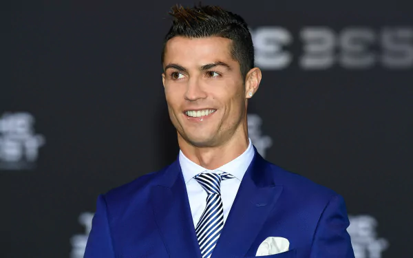 Cristiano Ronaldo, the Portuguese soccer star, smiles while wearing a blue suit and striped tie. The image serves as a high-definition desktop wallpaper and background.