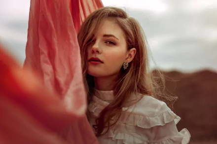 HD desktop wallpaper of a brunette woman with lipstick, posed gracefully against a flowing red fabric background. The serene model wears a stylish white blouse, creating a captivating and artistic visual.