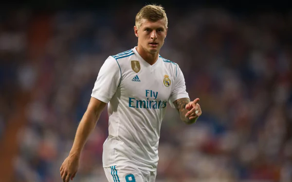 HD desktop wallpaper of German soccer player Toni Kroos in action, wearing a white Real Madrid jersey during a match.