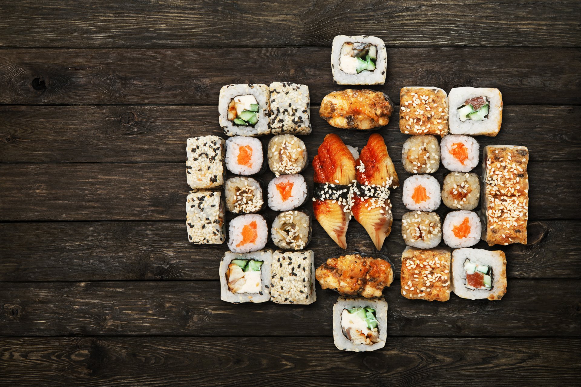 A vibrant assortment of sushi rolls with rice and seafood arranged on a dark wooden surface, captured in 4K Ultra HD for a crisp, detailed still life food wallpaper.