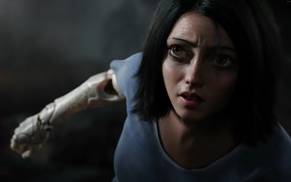 Alita from the movie Alita: Battle Angel gazes intently, her mechanical arm slightly raised. This HD desktop wallpaper captures the essence of the character's determination and strength.