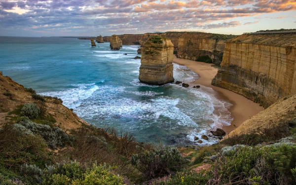 Scenic view of The Twelve Apostles along the rugged Australian coastline with ocean waves crashing against dramatic cliffs under a colorful sky.