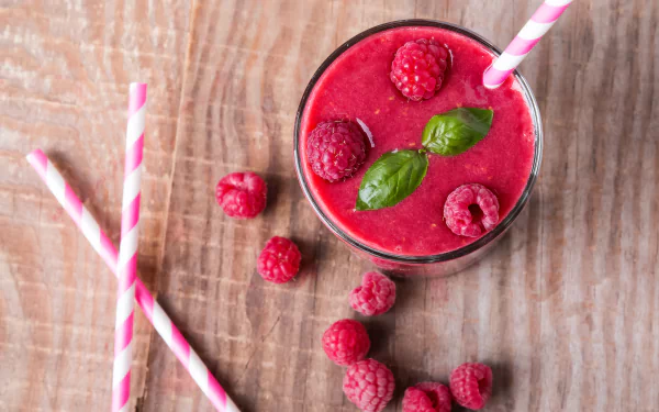 4K Ultra HD still-life of a raspberry smoothie in a glass with basil leaves and a striped straw, scattered raspberries on a wooden background — food/drink PC desktop wallpaper.