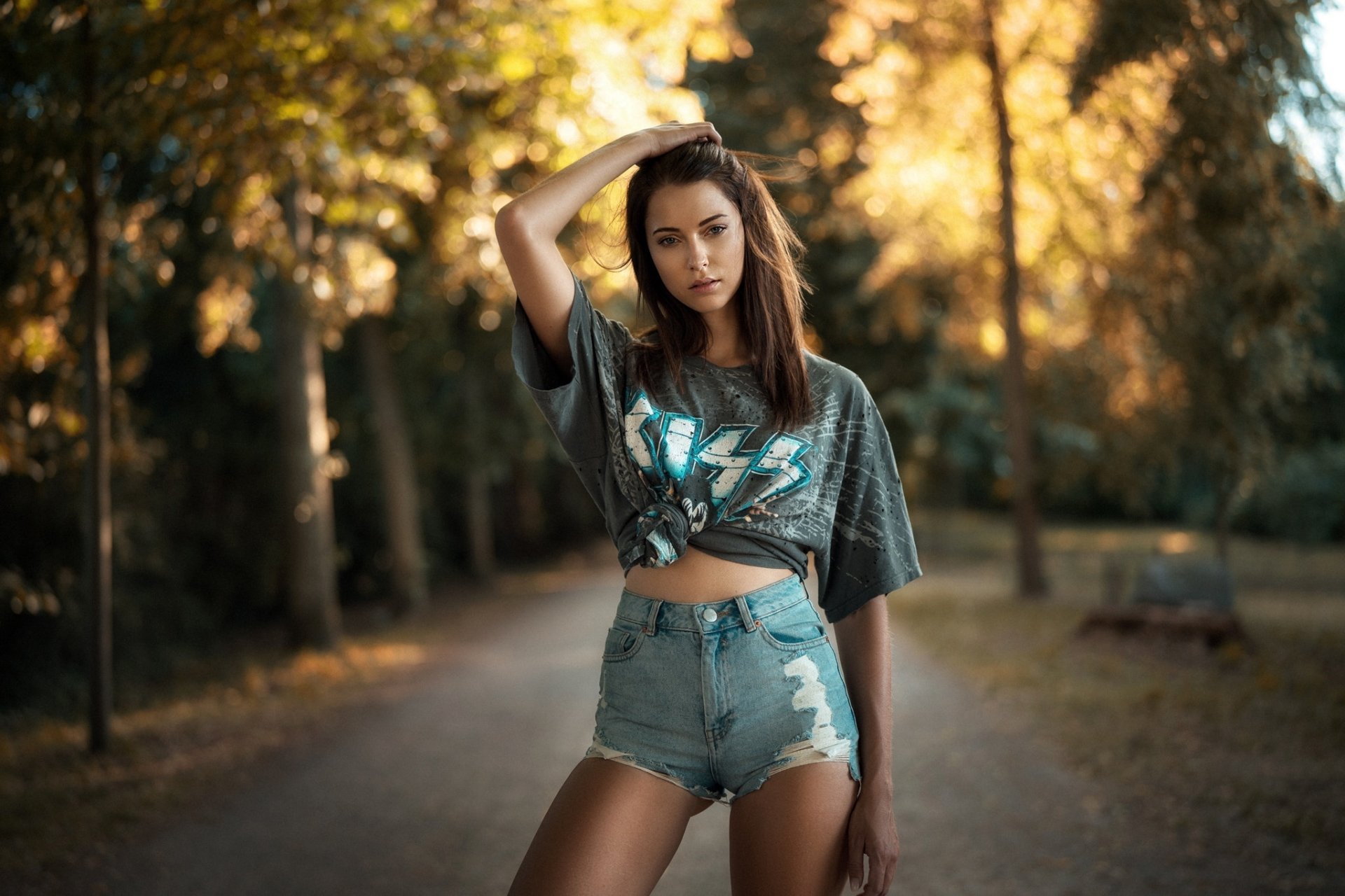 A brunette woman model poses outdoors wearing distressed shorts and a graphic tee, captured with a shallow depth of field in this HD PC desktop wallpaper background.