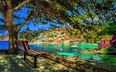 A tranquil coastal village in Greece, featuring colorful buildings by the water, lush greenery, and a serene bench overlooking the bay. A stunning 4K Ultra HD wallpaper.