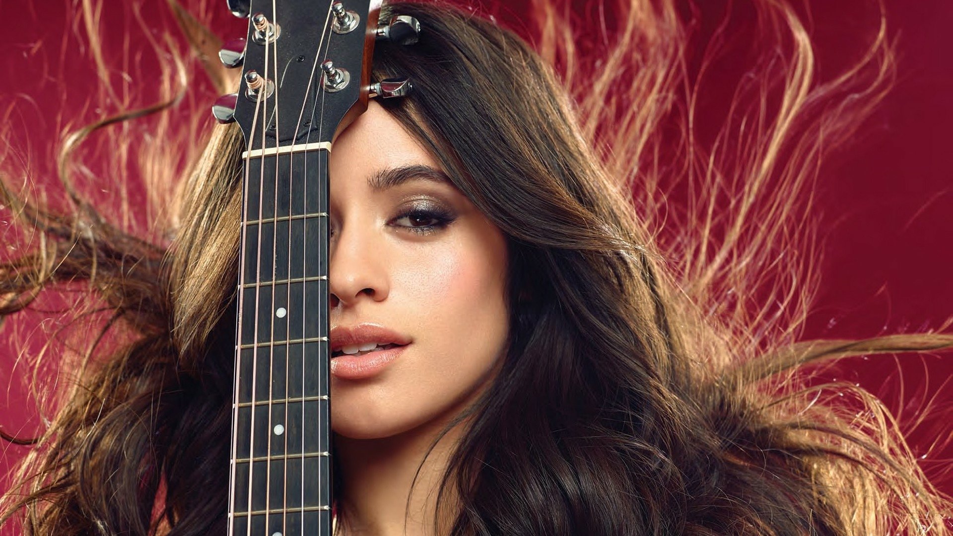 HD desktop wallpaper of a brunette Latina singer with brown eyes holding a guitar, featuring Camila Cabello against a vibrant red background.