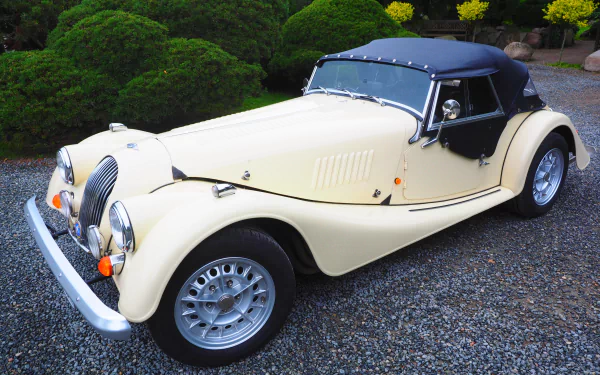 A cream-colored vintage Morgan Plus 8 roadster parked on gravel, captured in a detailed 4K Ultra HD PC wallpaper and background image.