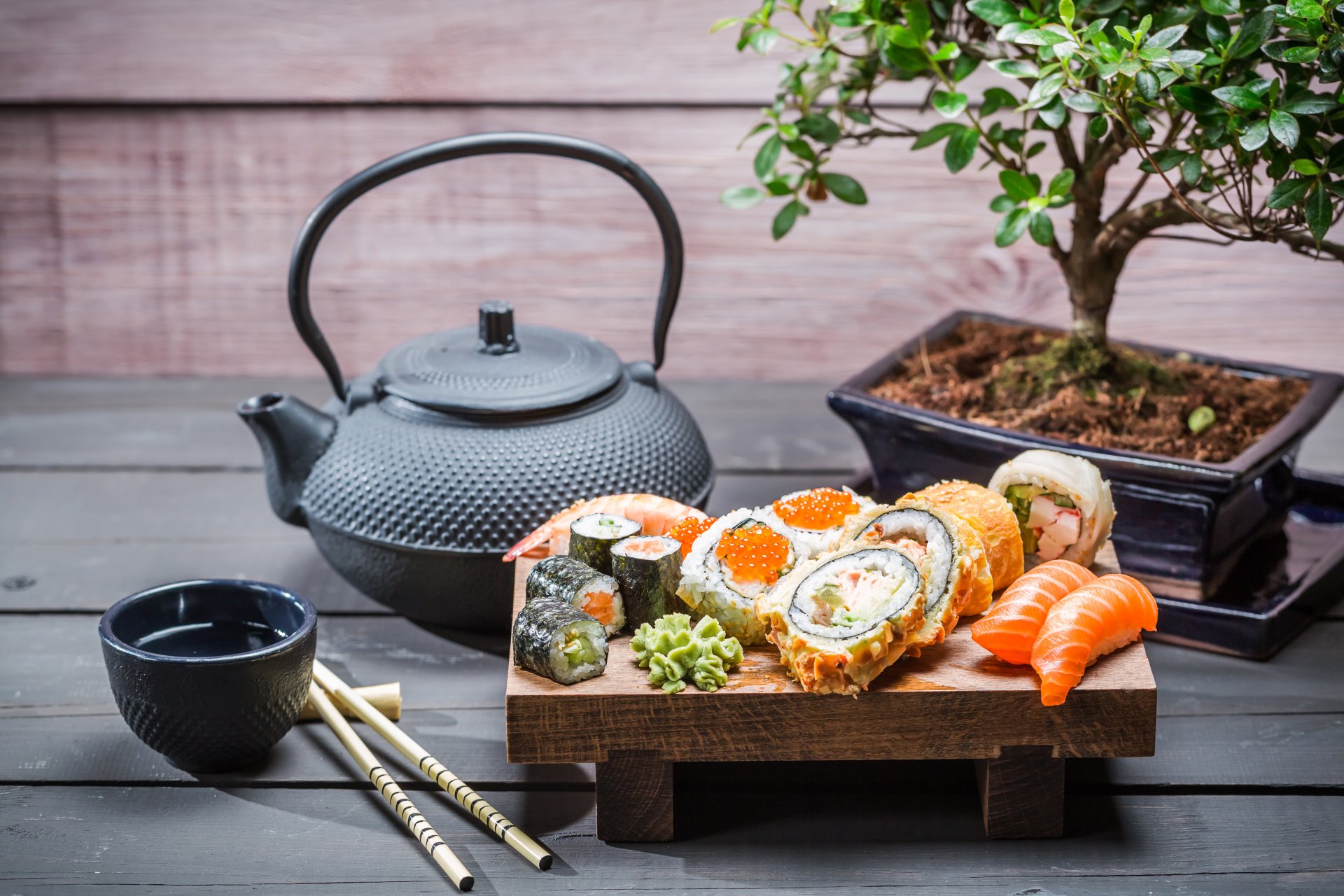 A 4K Ultra HD still life featuring sushi and seafood arranged on a wooden tray, accompanied by a black teapot, teacup, chopsticks, and a bonsai tree on a wooden surface.