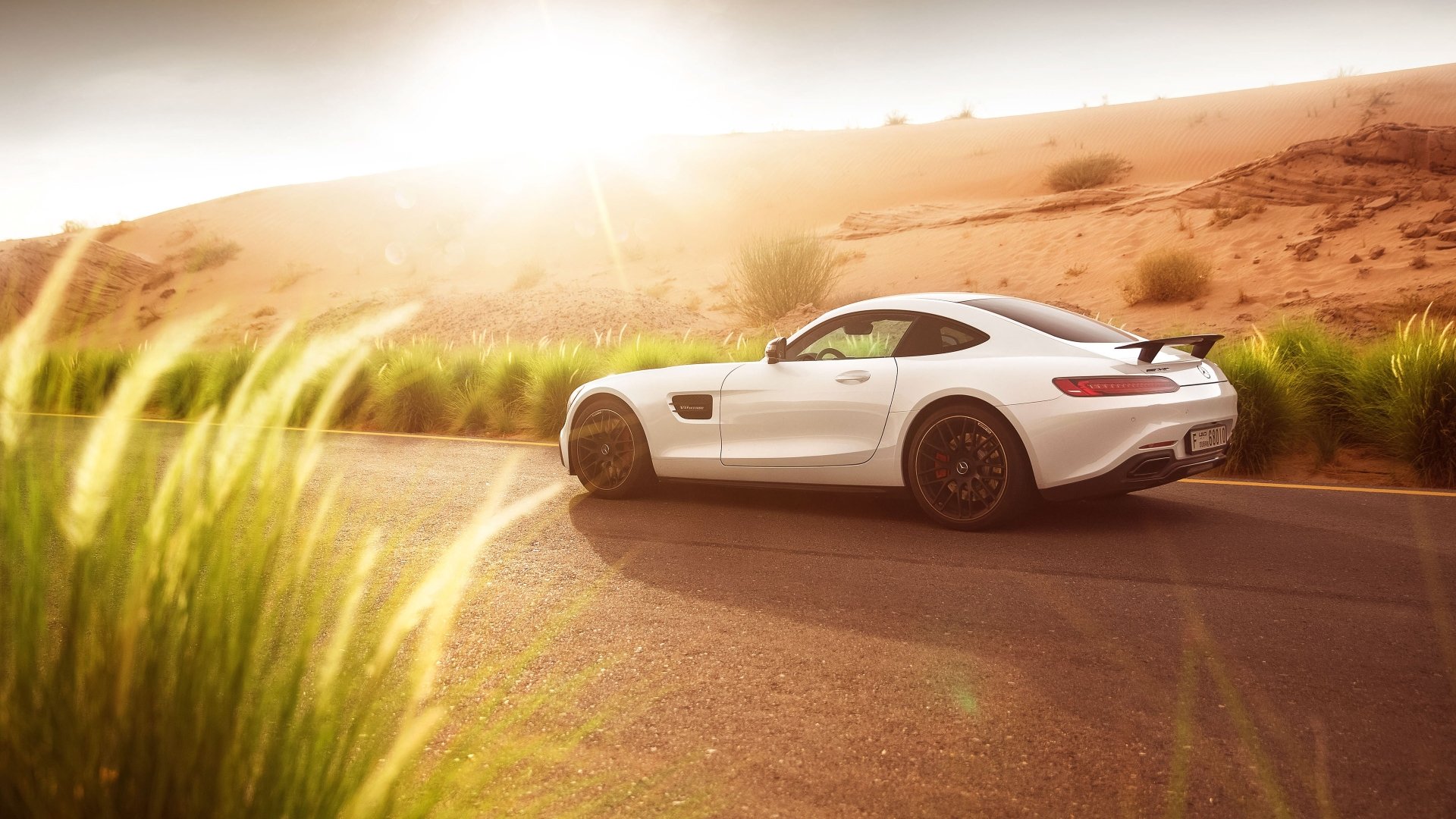 A white Mercedes-AMG GT S supercar driving on a sunlit desert road, captured in stunning 4K Ultra HD for a dynamic PC desktop wallpaper.