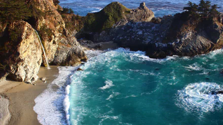HD desktop wallpaper of McWay Falls in Big Sur, California, showing the waterfall cascading down a cliff onto a pristine beach by the vibrant, turquoise coastal waters. Lush greenery tops the rugged cliffs.