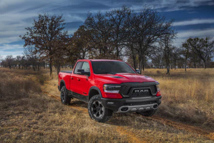HD desktop wallpaper featuring a red Dodge Ram 1500 truck parked in a grassy field with leafless trees under a partly cloudy sky.