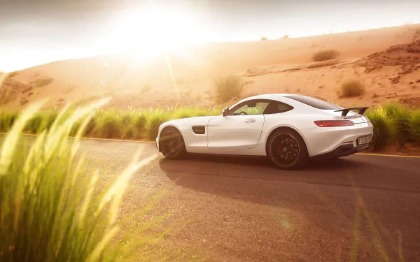 A white Mercedes-AMG GT S supercar driving on a sunlit desert road, captured in stunning 4K Ultra HD for a dynamic PC desktop wallpaper.