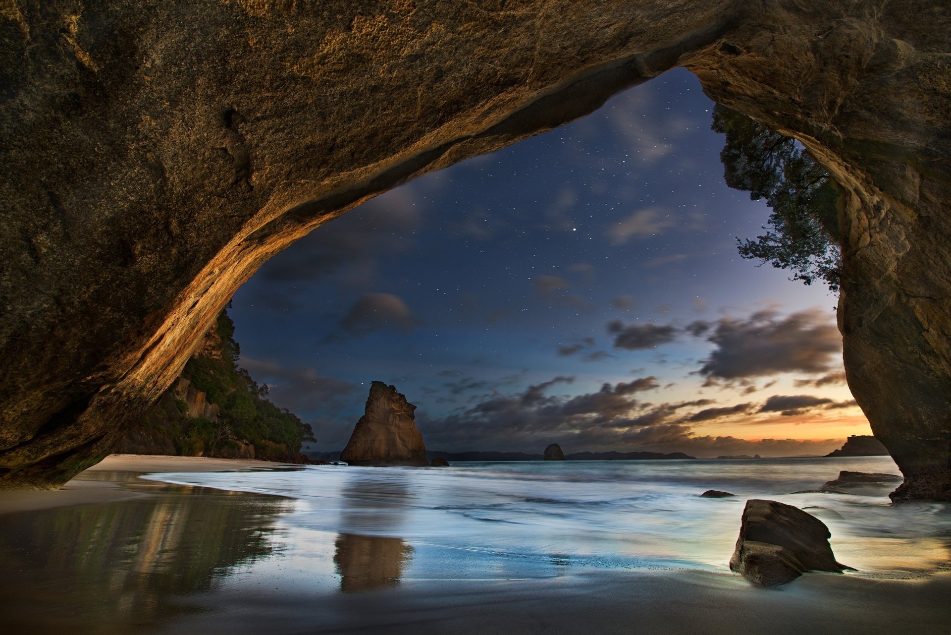 A serene night scene of a cave opening showcasing a coastal landscape, with gentle waves reflecting the twilight sky amid lush greenery, capturing the essence of nature. HD PC wallpaper.