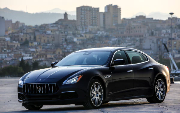 Black Maserati Quattroporte sedan parked by a waterfront with a city skyline, presented as a 4K Ultra HD PC desktop wallpaper/background.