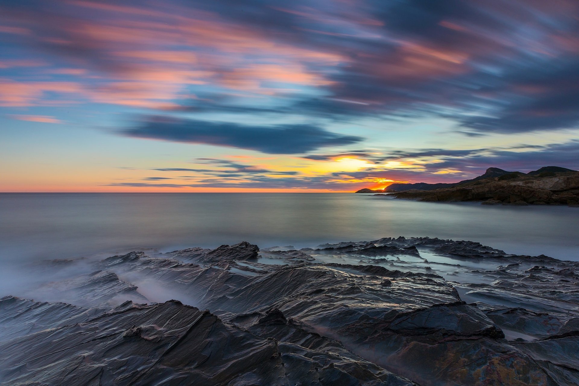 HD PC desktop wallpaper showcasing a serene ocean horizon at sunset with vibrant skies and rocky shore under soft, colorful clouds in a nature setting.