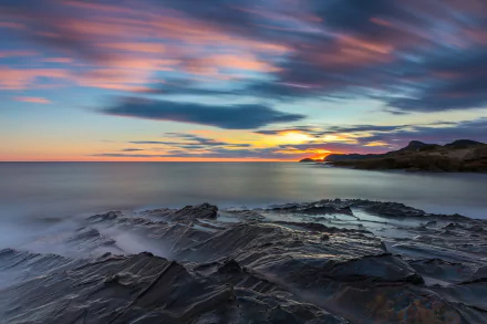 HD PC desktop wallpaper showcasing a serene ocean horizon at sunset with vibrant skies and rocky shore under soft, colorful clouds in a nature setting.