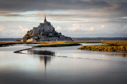 Mont Saint-Michel rises majestically above a serene landscape in France, reflecting in the tranquil waters, showcasing its stunning religious architecture and natural beauty.