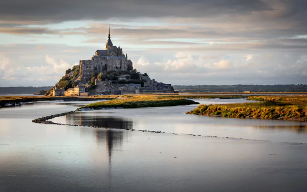 Mont Saint-Michel rises majestically above a serene landscape in France, reflecting in the tranquil waters, showcasing its stunning religious architecture and natural beauty.