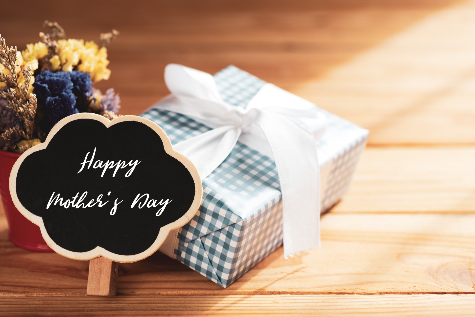 Happy Mother's Day chalkboard beside a plaid-wrapped gift with white bow on a wooden table — 5K Ultra HD PC desktop wallpaper background for Mother's Day holiday.