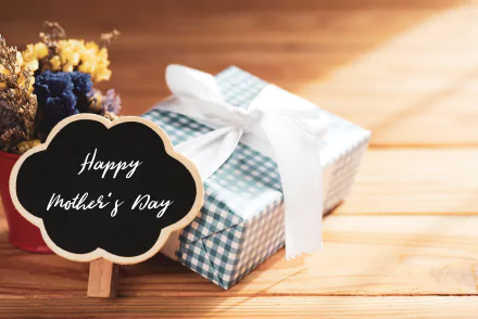 Happy Mother's Day chalkboard beside a plaid-wrapped gift with white bow on a wooden table — 5K Ultra HD PC desktop wallpaper background for Mother's Day holiday.