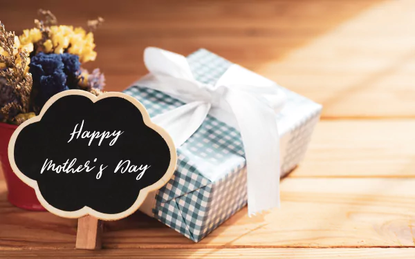 Happy Mother's Day chalkboard beside a plaid-wrapped gift with white bow on a wooden table — 5K Ultra HD PC desktop wallpaper background for Mother's Day holiday.