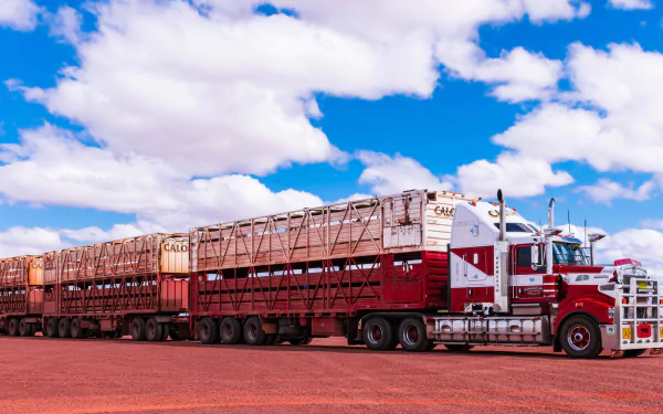 A Kenworth road train with multiple trailers parked on a red dirt road under a bright blue sky with scattered clouds, captured in 4K Ultra HD quality.