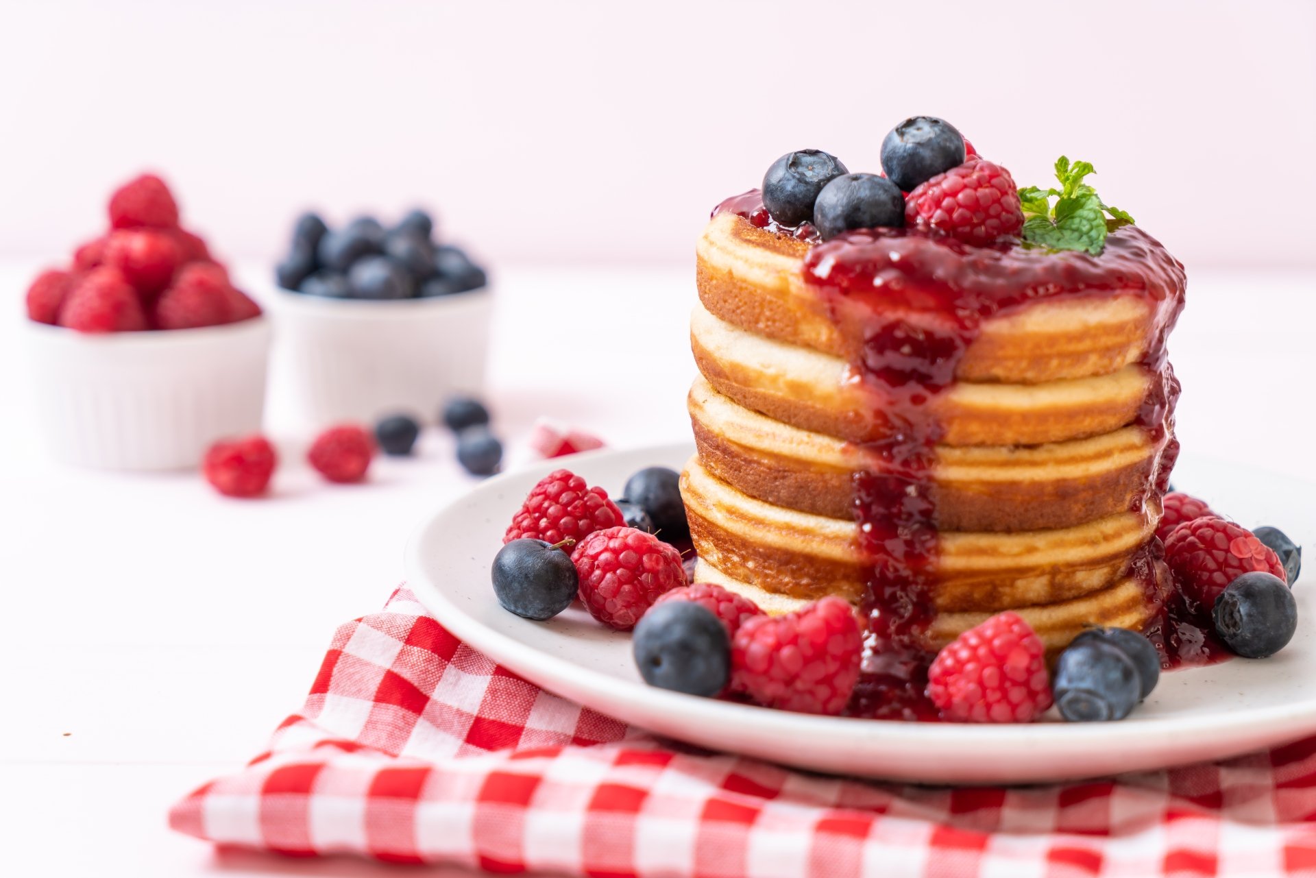 Stack of pancakes topped with raspberry and blueberry jam and fresh berries, set on a red checkered cloth, captured in 8K Ultra HD as a still life breakfast scene.