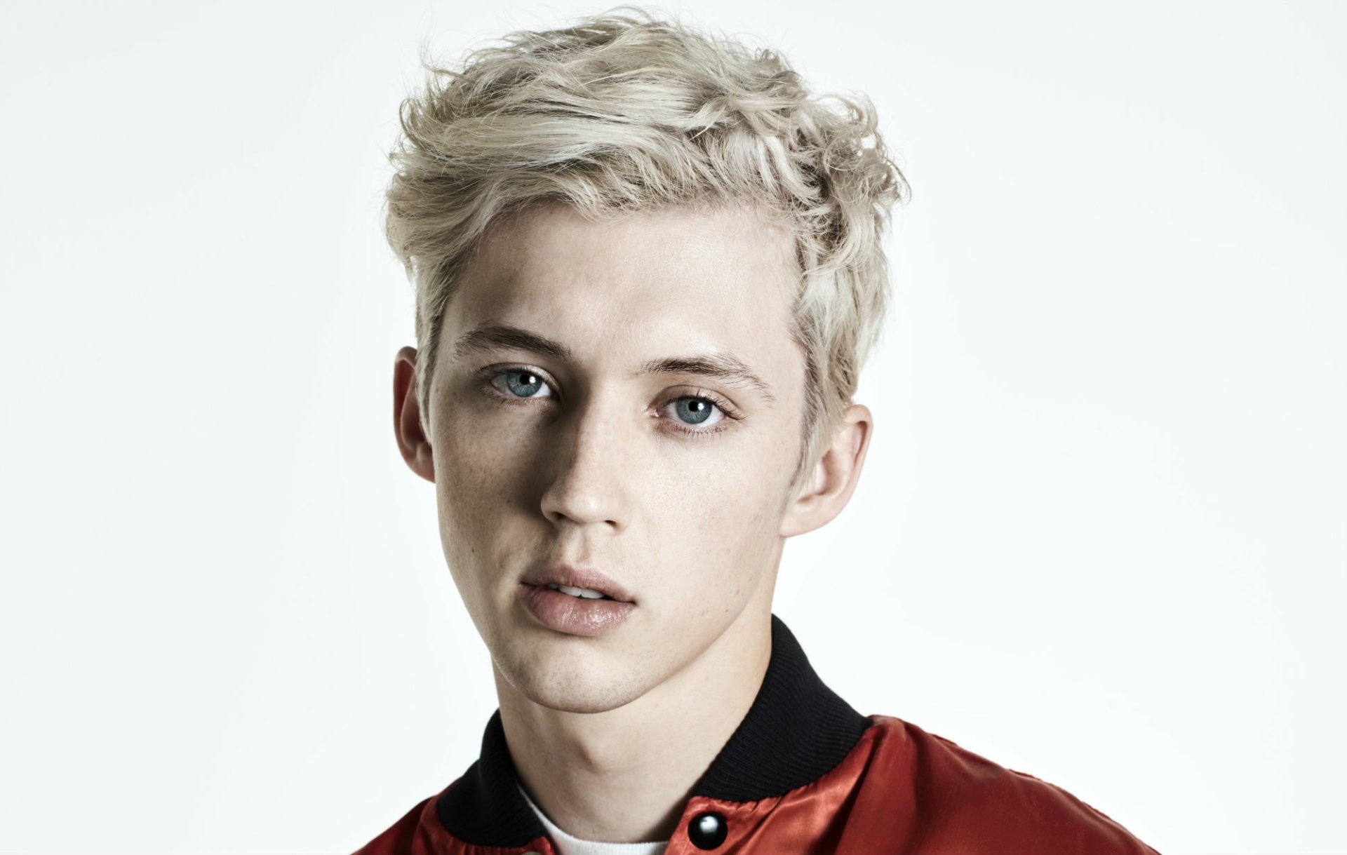 HD desktop wallpaper featuring a portrait of a person with platinum blonde hair and blue eyes, wearing a red and black shirt.