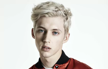 HD desktop wallpaper featuring a portrait of a person with platinum blonde hair and blue eyes, wearing a red and black shirt.