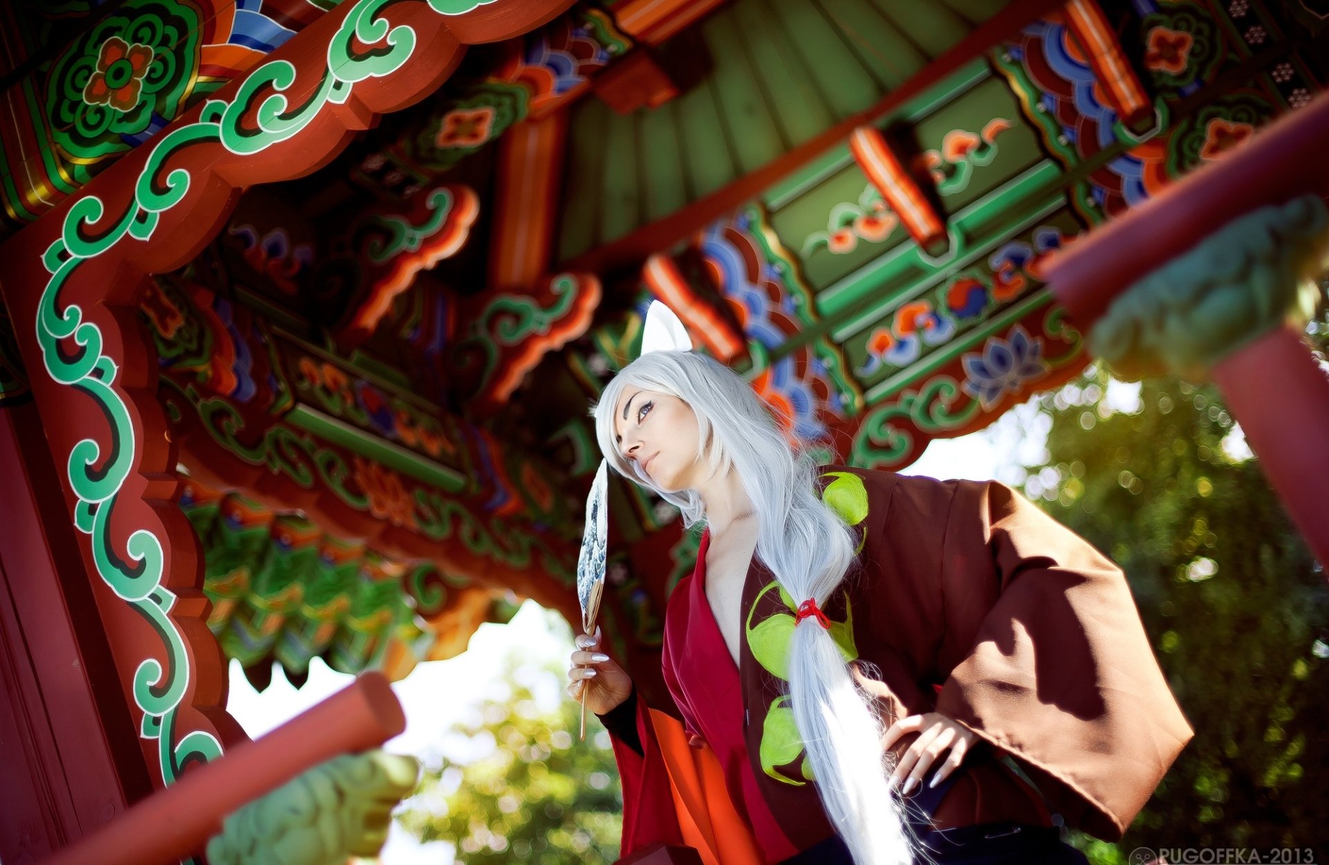 HD desktop wallpaper: male cosplayer as Tomoe (Kamisama Kiss) in white wig and kimono, posed beneath an ornate pagoda with vivid decorative roof and sunlit background.