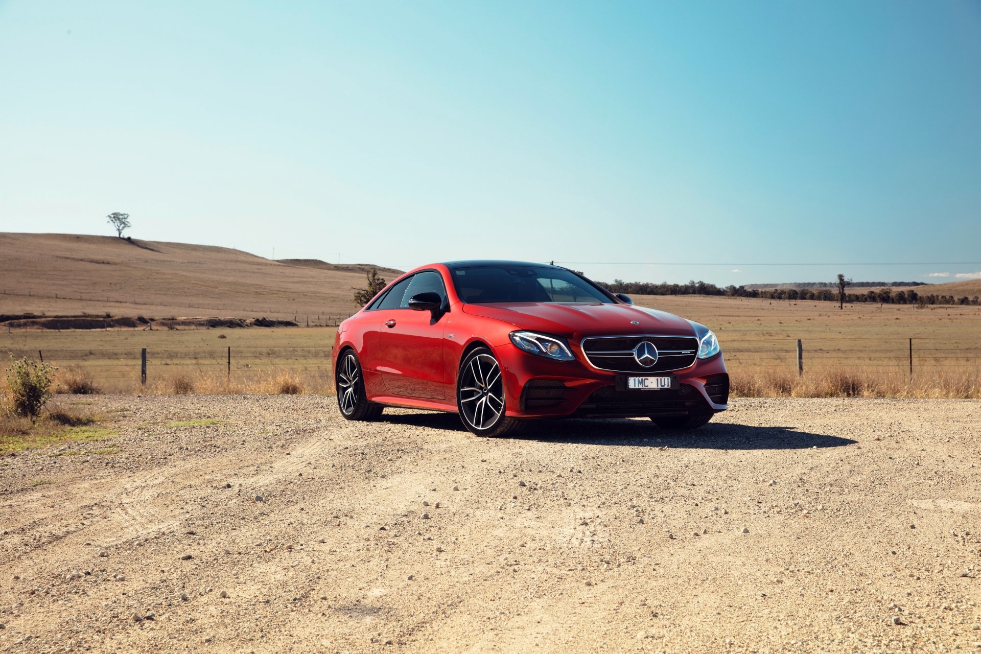 Red Mercedes-Benz E-Class coupe parked on a gravel road in open countryside, 4K Ultra HD PC desktop wallpaper of a Mercedes-Benz car/vehicle.